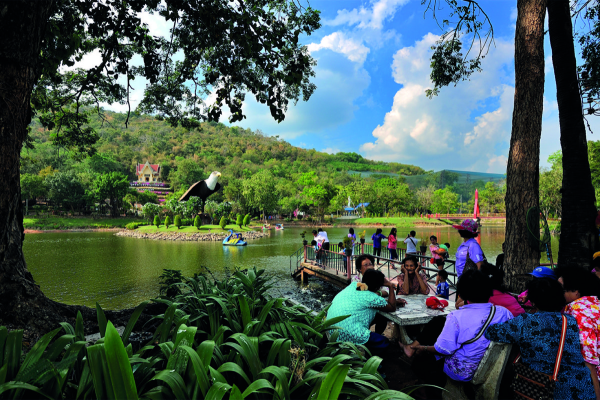 2015年猜纳鸟园水岸，近处游客坐在树下，平台伸入水面，对岸是鹰形雕塑和山坡