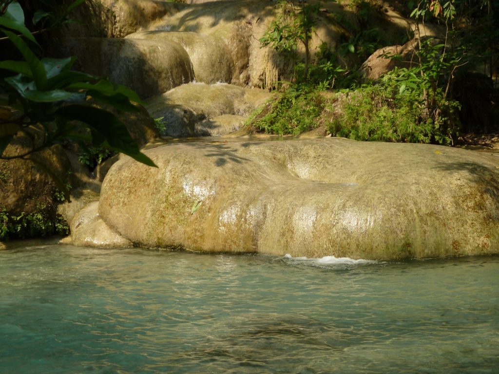 爱侣湾瀑布上层水流越过浅色石灰岩，汇入蓝绿色水面