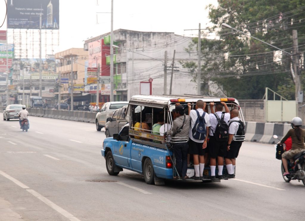 芭提雅城市道路上一辆蓝色双条车载着穿校服的乘客，数人站在后踏板
