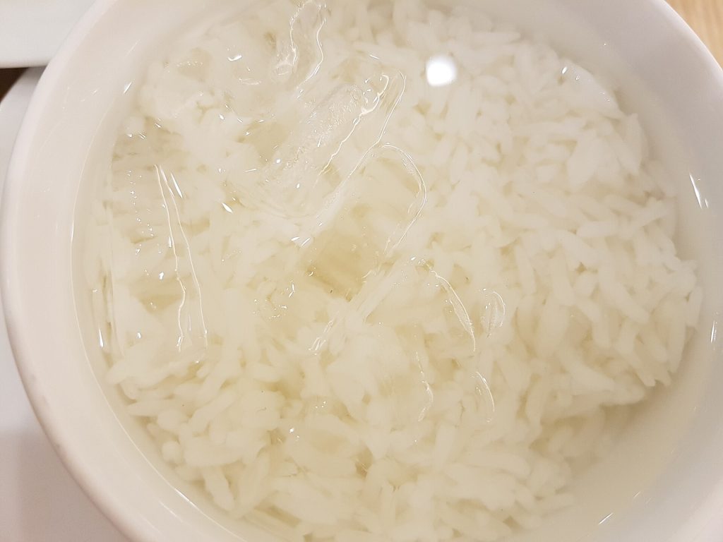 白色圆碗中装着粒粒分明的米饭、清水与正在融化的透明冰块