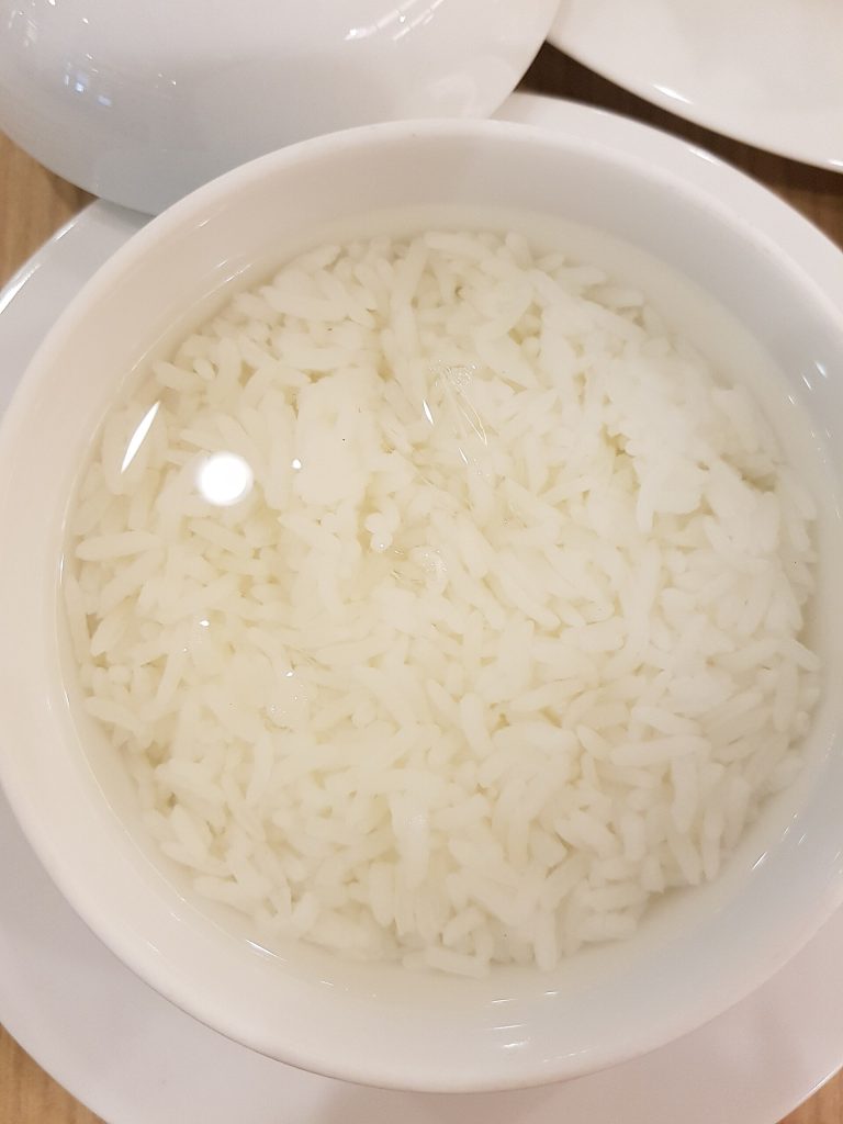 近距离俯拍白色饭碗，长形米粒浸在透明花香水中