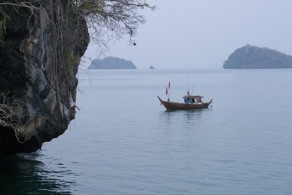 达鲁岛深色海岸岩壁、小船与远处岛屿