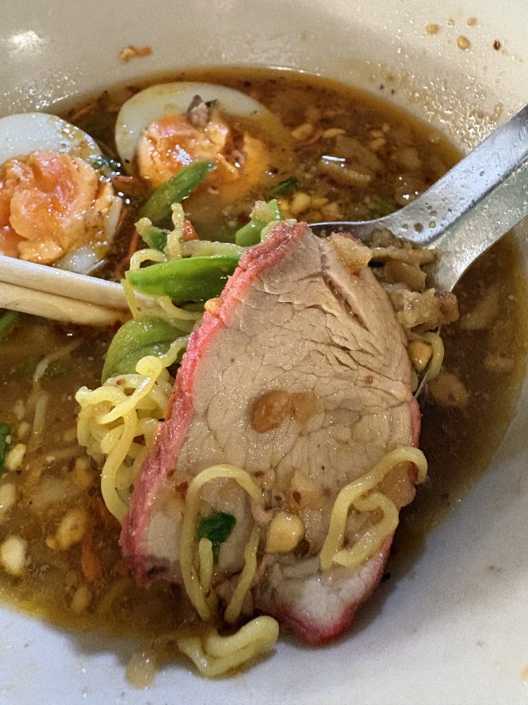 素可泰汤面近景中的红边猪肉片、黄面、长豆、花生碎与深色汤汁
