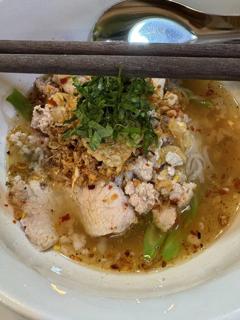 白色米粉上的猪肉片、肉末、碎花生、香草与绿色长豆近景