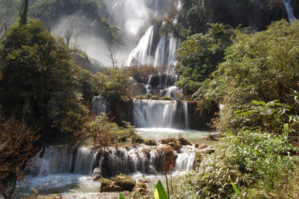 提洛苏瀑布多级水帘穿过浓密绿树并流向前景岩石