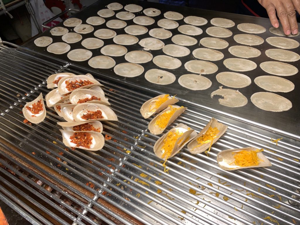 摊主在大铁板上摊开数十个小圆饼壳，旁边放着甜咸两类成品