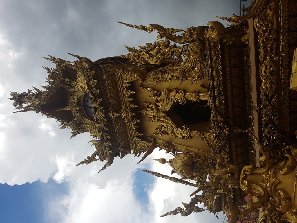 低角度拍摄的清莱金色钟楼雕饰与街口天空