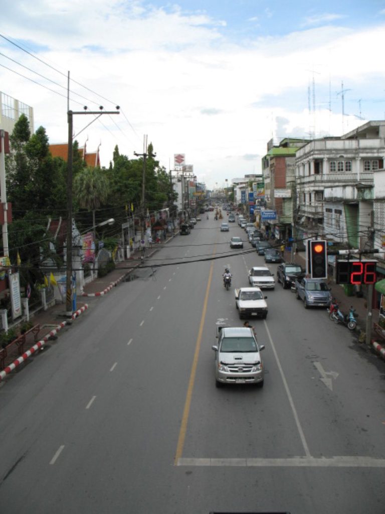 洛坤市区一条双向道路，两侧有商铺、电线和行道树