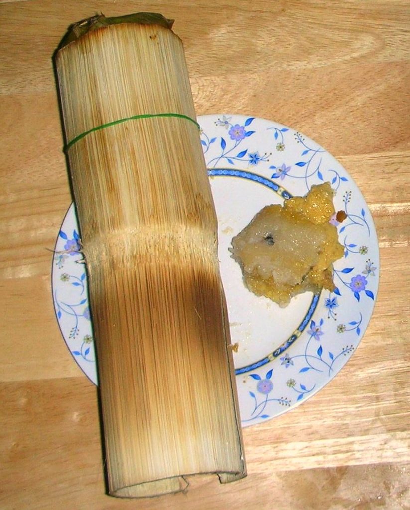 一支表面烤焦的竹筒饭放在盘中,旁边摆着一小份糯米