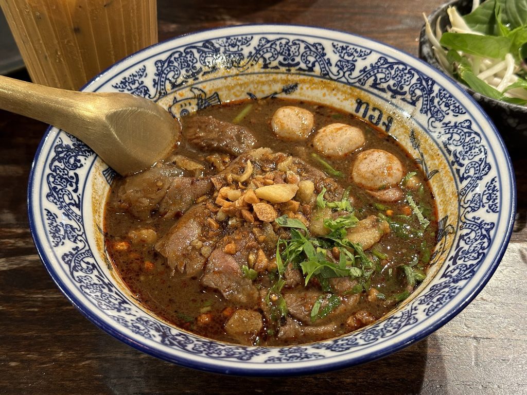 蓝白花纹碗中有深色汤、牛肉片、牛肉丸、花生碎和香草