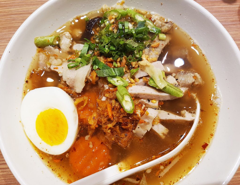 白碗中有清褐色酸辣面汤、猪肉片、半颗鸡蛋、青菜和辣椒调料