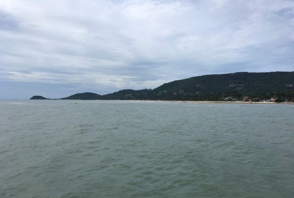 从海上接近苏梅岛时看到的绿色山坡、沿岸建筑与灰蓝色海面