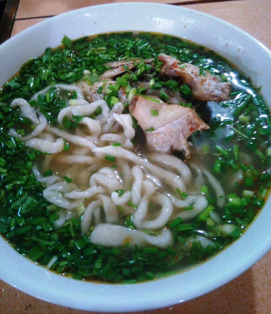 白碗里盛着粗短白面条、鱼肉块、肉丸与大量绿色香草