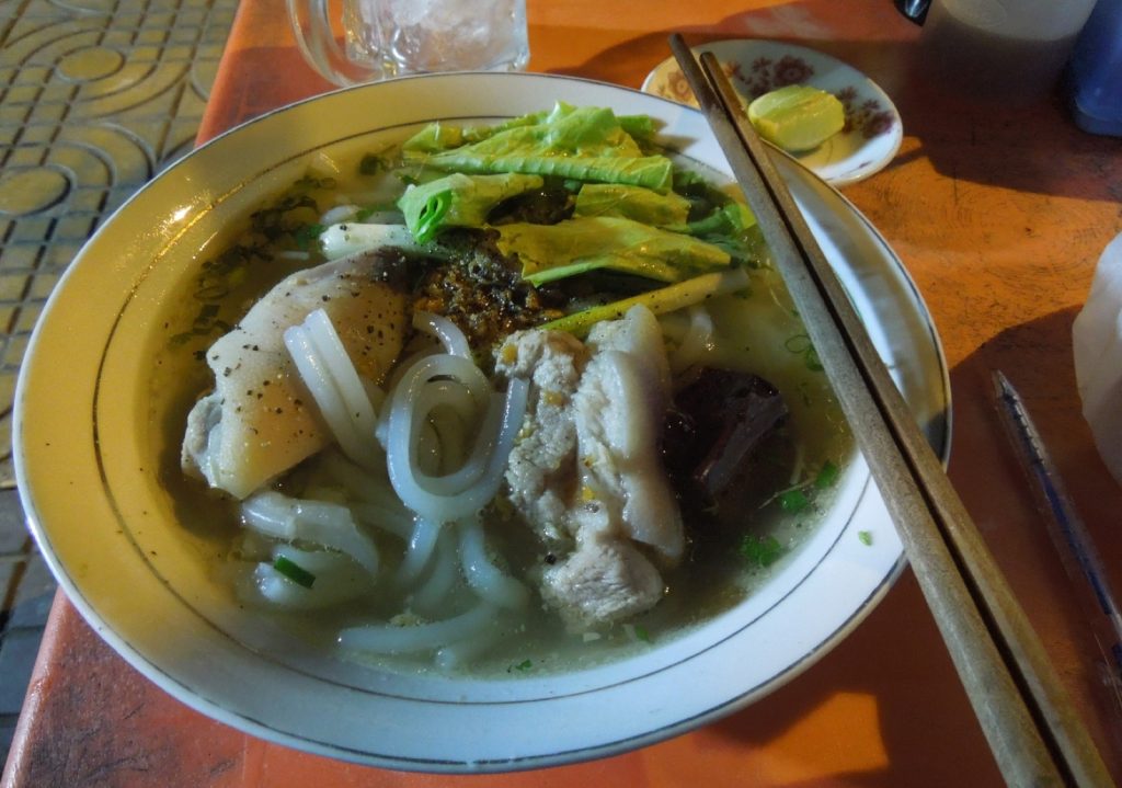 桌上一碗粗圆白面条清汤配有猪肉、血块、生菜和胡椒