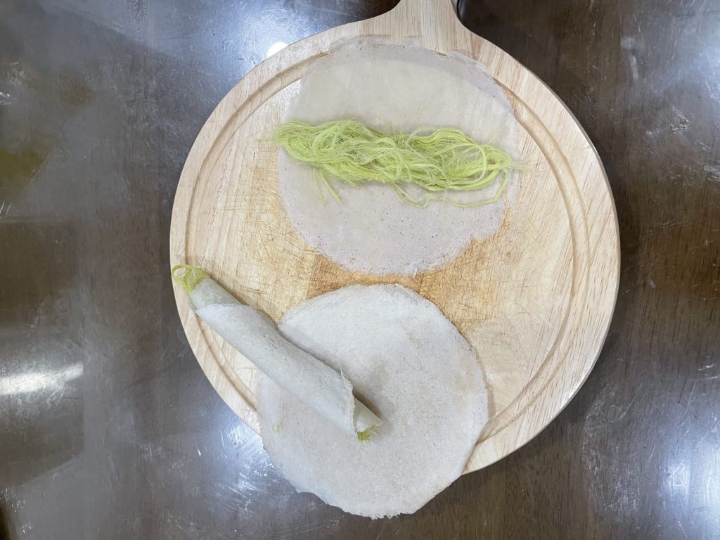 木盘上的一张薄饼铺着糖丝，旁边放着卷好的饼