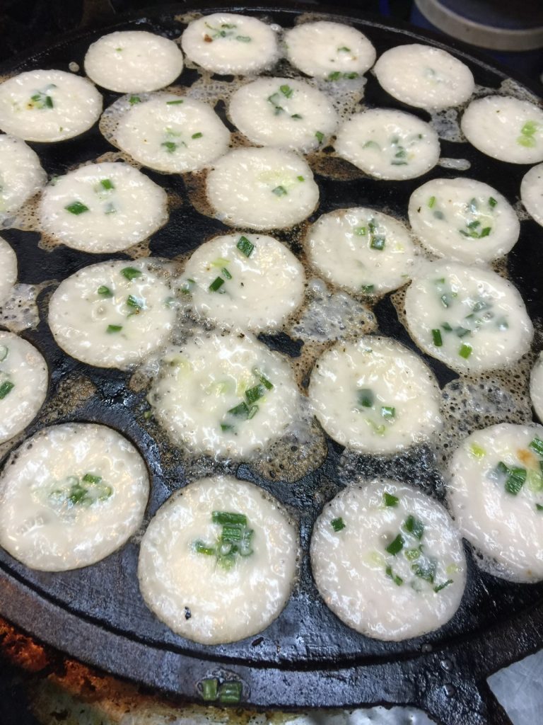 圆孔锅里撒着葱花的白色卡农克椰浆小饼