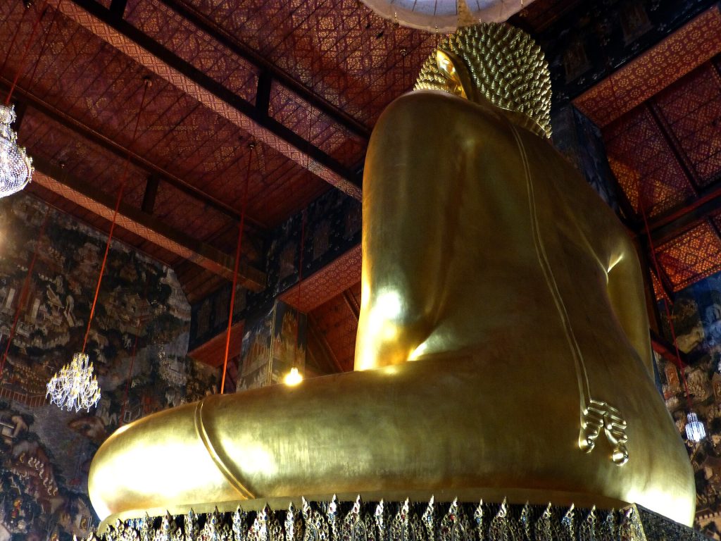 从侧后方仰望苏泰寺主佛殿内的大型金色坐佛，背后和两侧墙面布满叙事壁画。