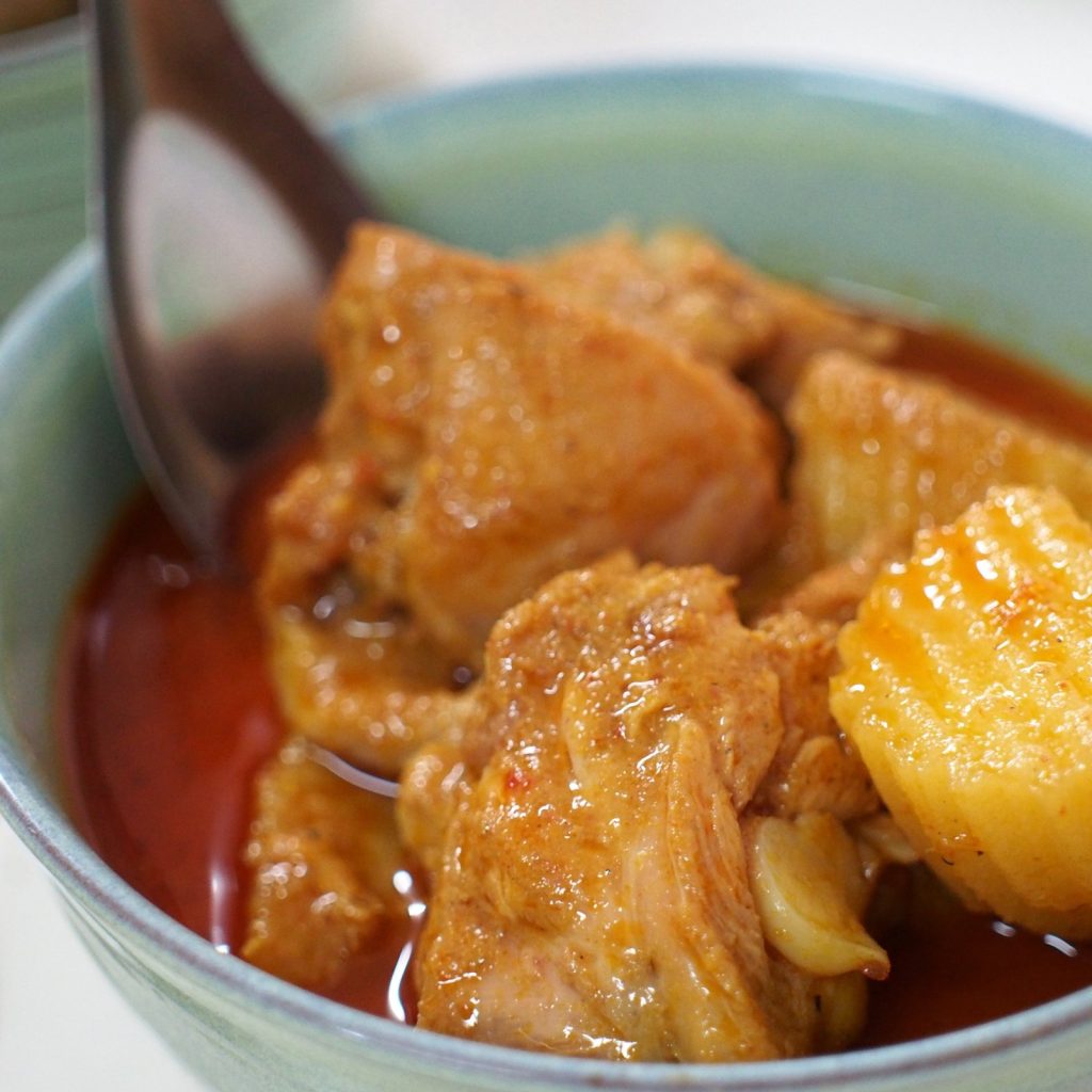 绿碗中的鸡肉土豆咖喱与餐勺