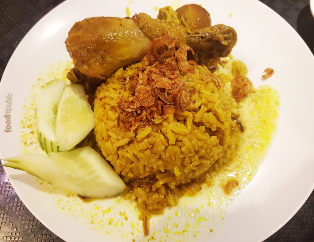白盘上的黄色香料饭、带骨鸡腿、炸红葱和黄瓜片
