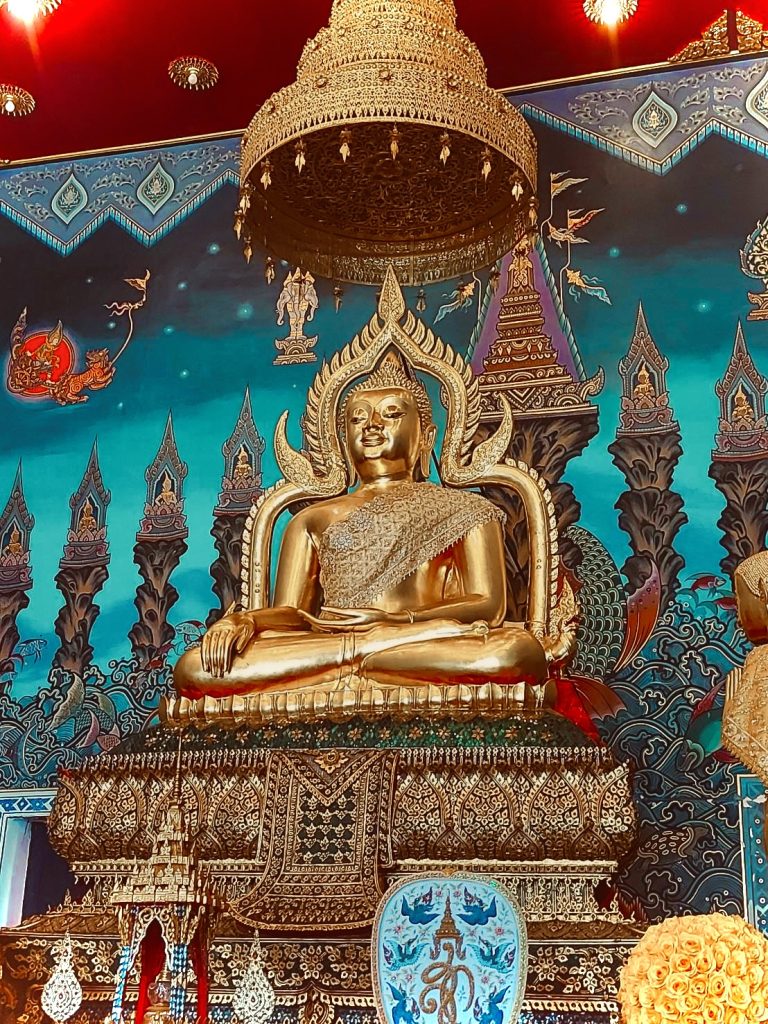 披集达銮寺佛殿内金色坐佛安奉在华盖下，背景是蓝绿色传统纹饰壁面