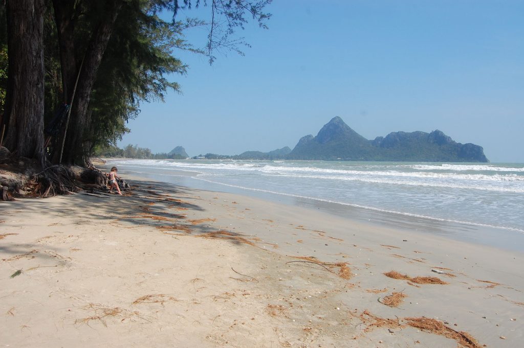 奥玛瑙湾沙滩一侧有高大树木遮阴，远处山体隔着浅蓝海面