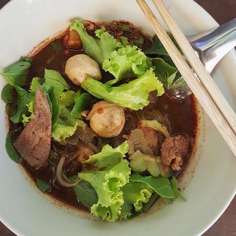 俯拍白碗里的泰式船面，汤中有肉丸、肉片和绿叶菜