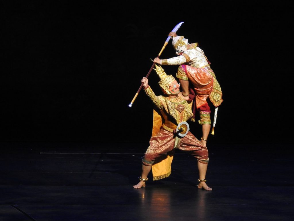 黑色舞台上两名戴面具演员做托举对抗姿势，上方演员持长杆，下方演员屈膝支撑。