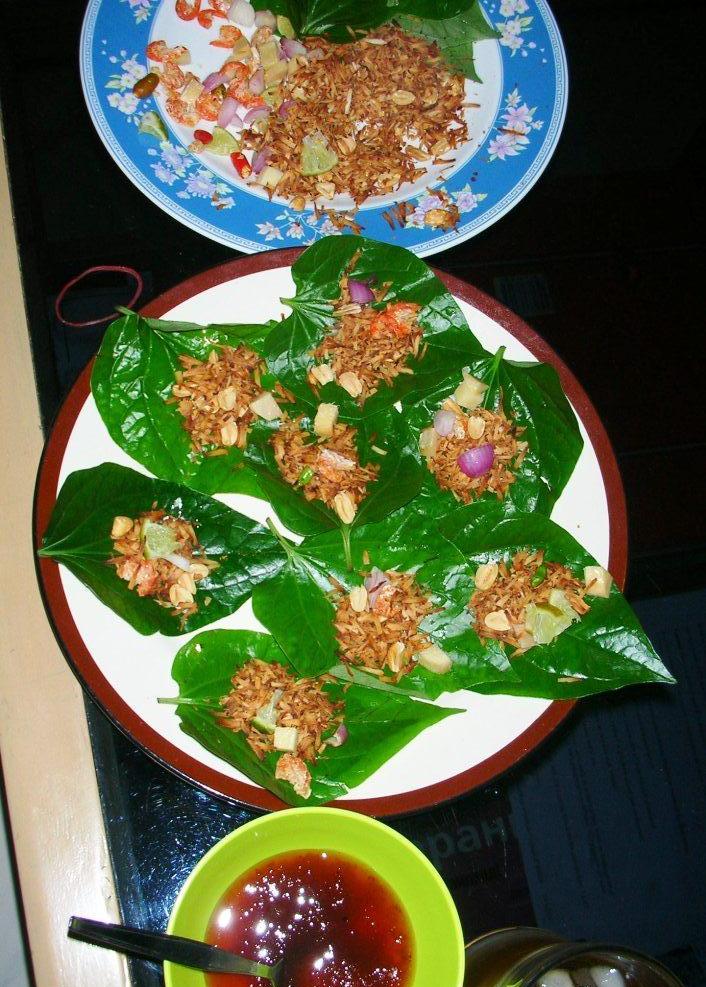 白盘上摆着多份已配好椰丝、花生等食材的 Miang Kham 叶包，旁边有酱汁