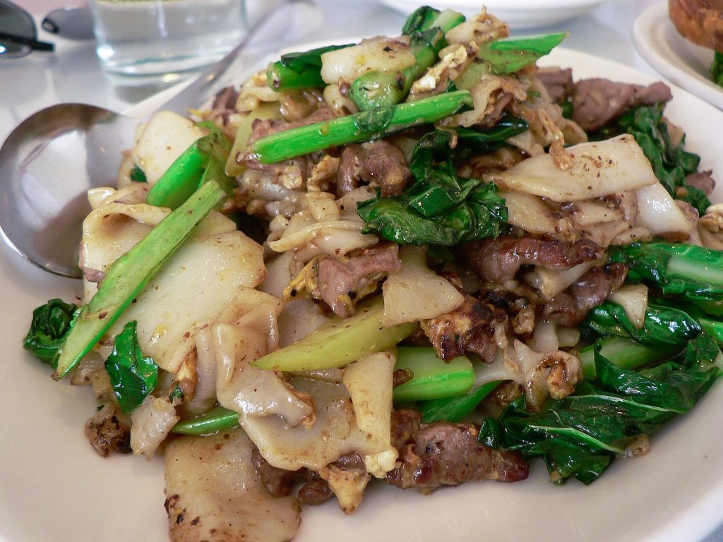 浅色宽粉、肉片与切开的绿色菜梗近景，粉面有褐色斑点。