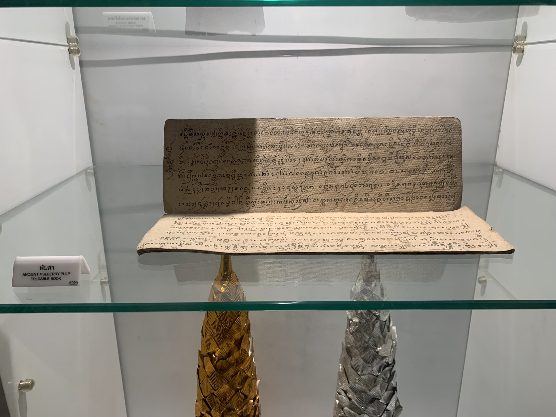 湄公河文明博物馆展柜中的 Phap Sa 桑纸折页书,纸面有多行手写文字。
