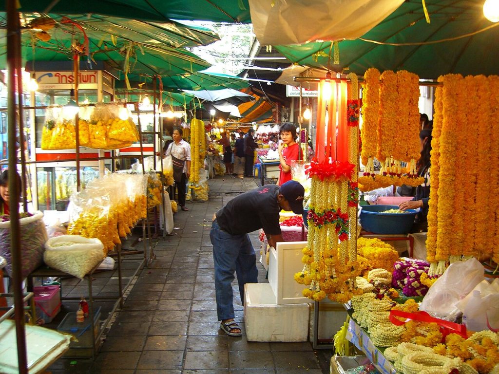 曼谷夜间花市里悬挂黄色花串，摊位上堆放白色花环