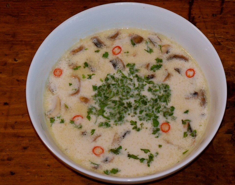 木桌上的椰奶鸡汤，汤面有蘑菇片和红椒圈