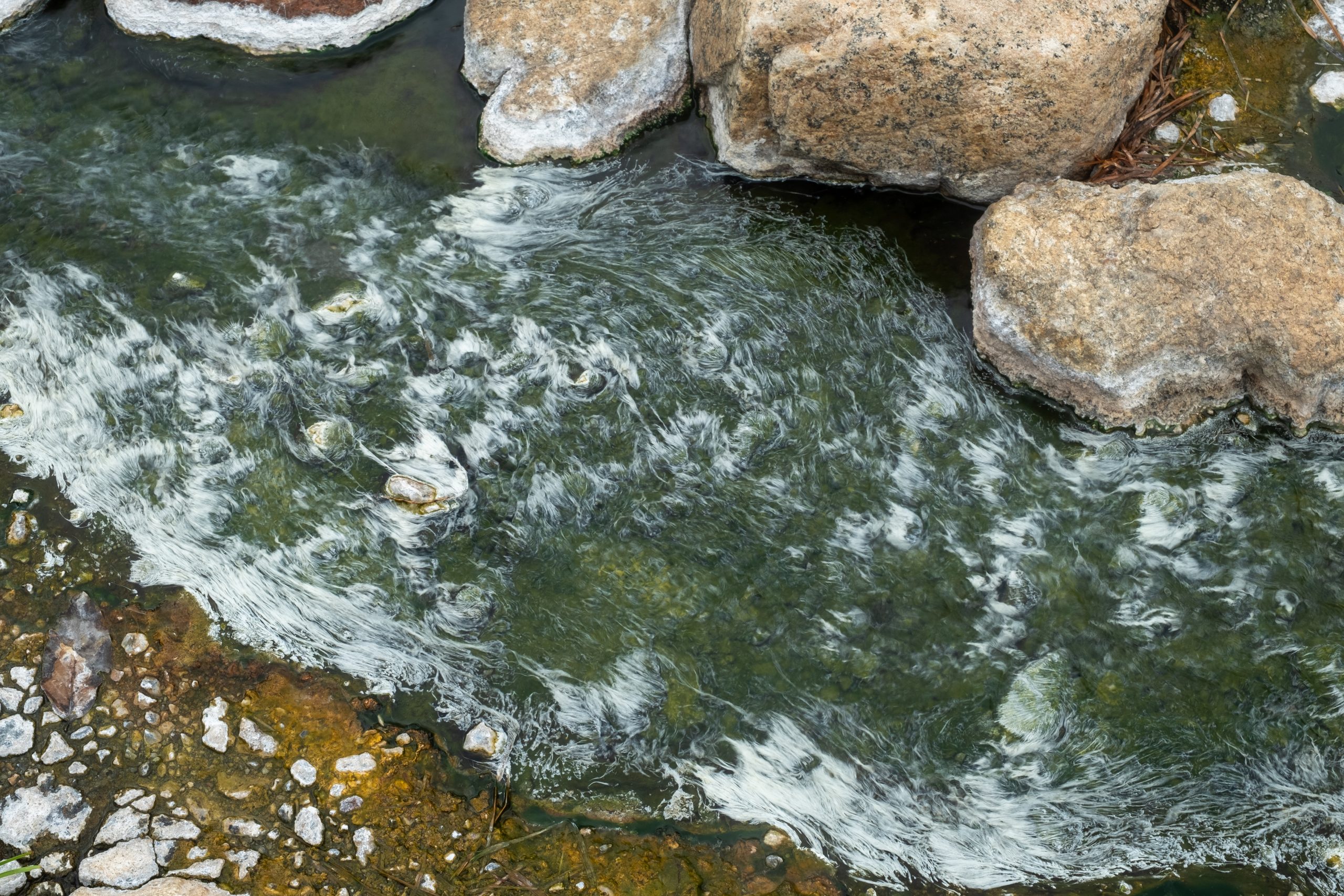 杰颂热泉水道俯视近景,水中小石子与浅色大岩块间有细密白色纹理,边缘有黄褐色部分