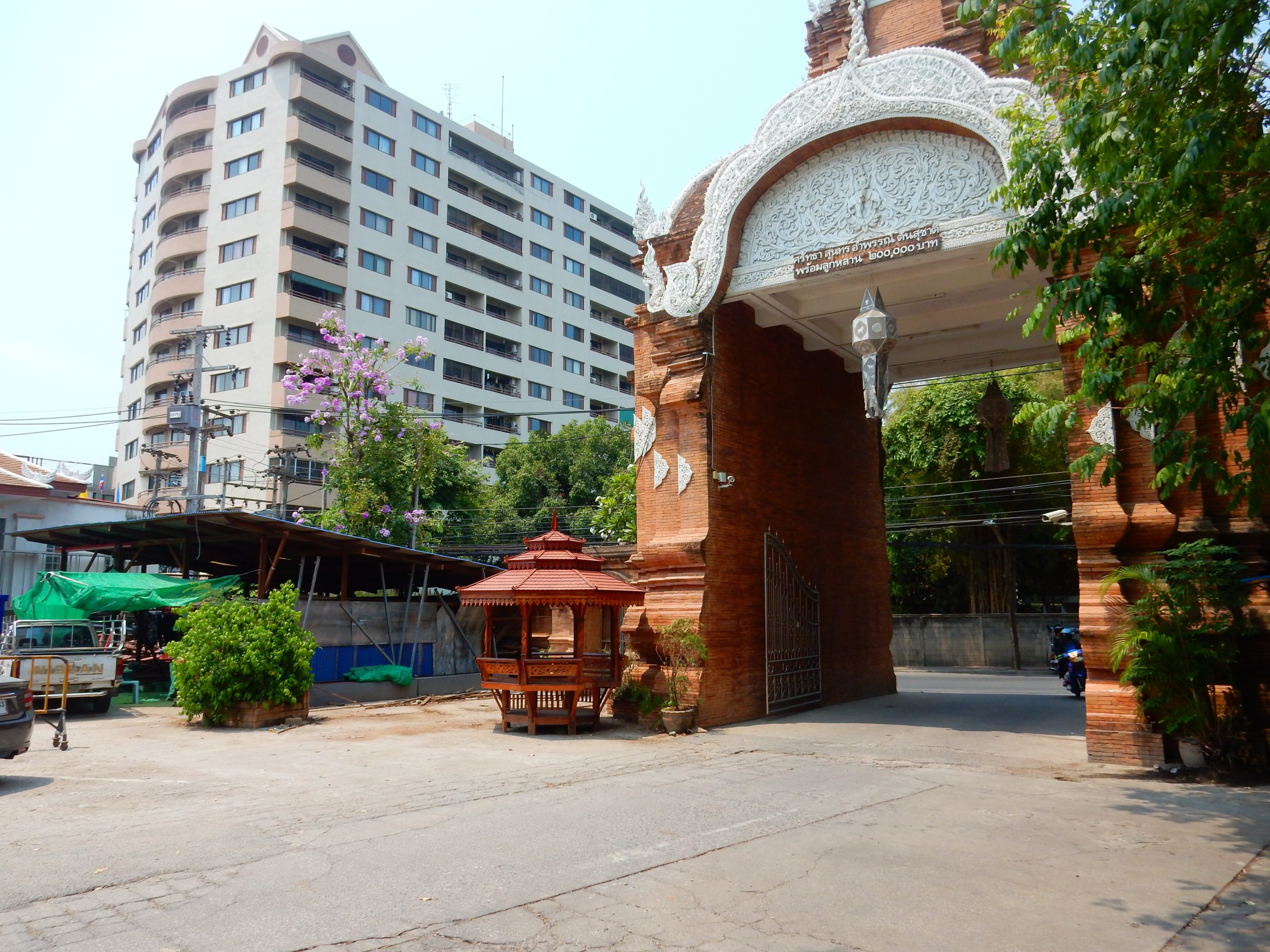 清迈 Wat Chai Mongkhon 砖砌门楼的白色弧形装饰，门洞朝向道路，左侧是高楼