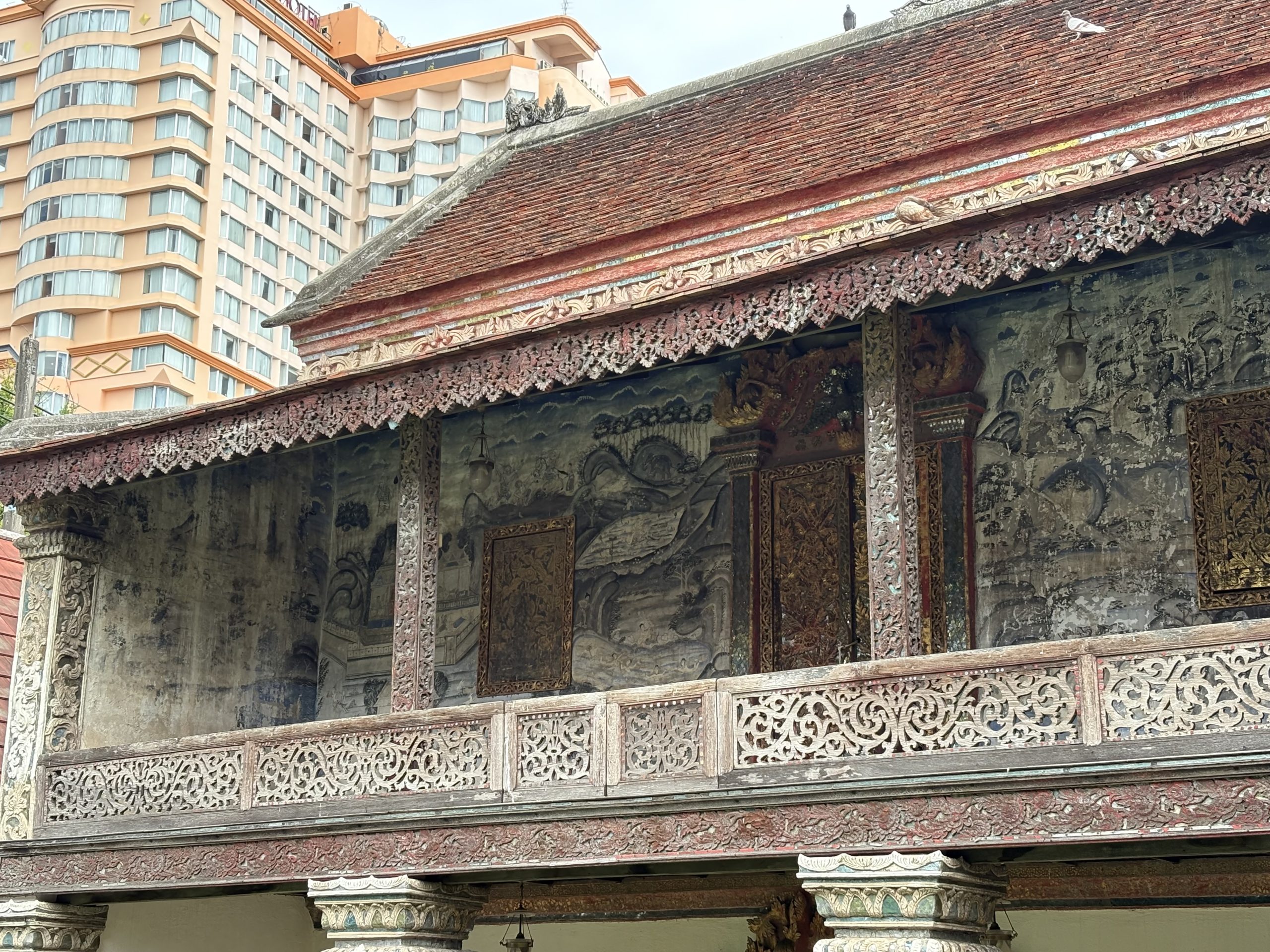 清迈 Wat Chang Khong 经楼上层左侧近照，金门两侧的壁画、木窗、花叶木栏及后方现代楼房