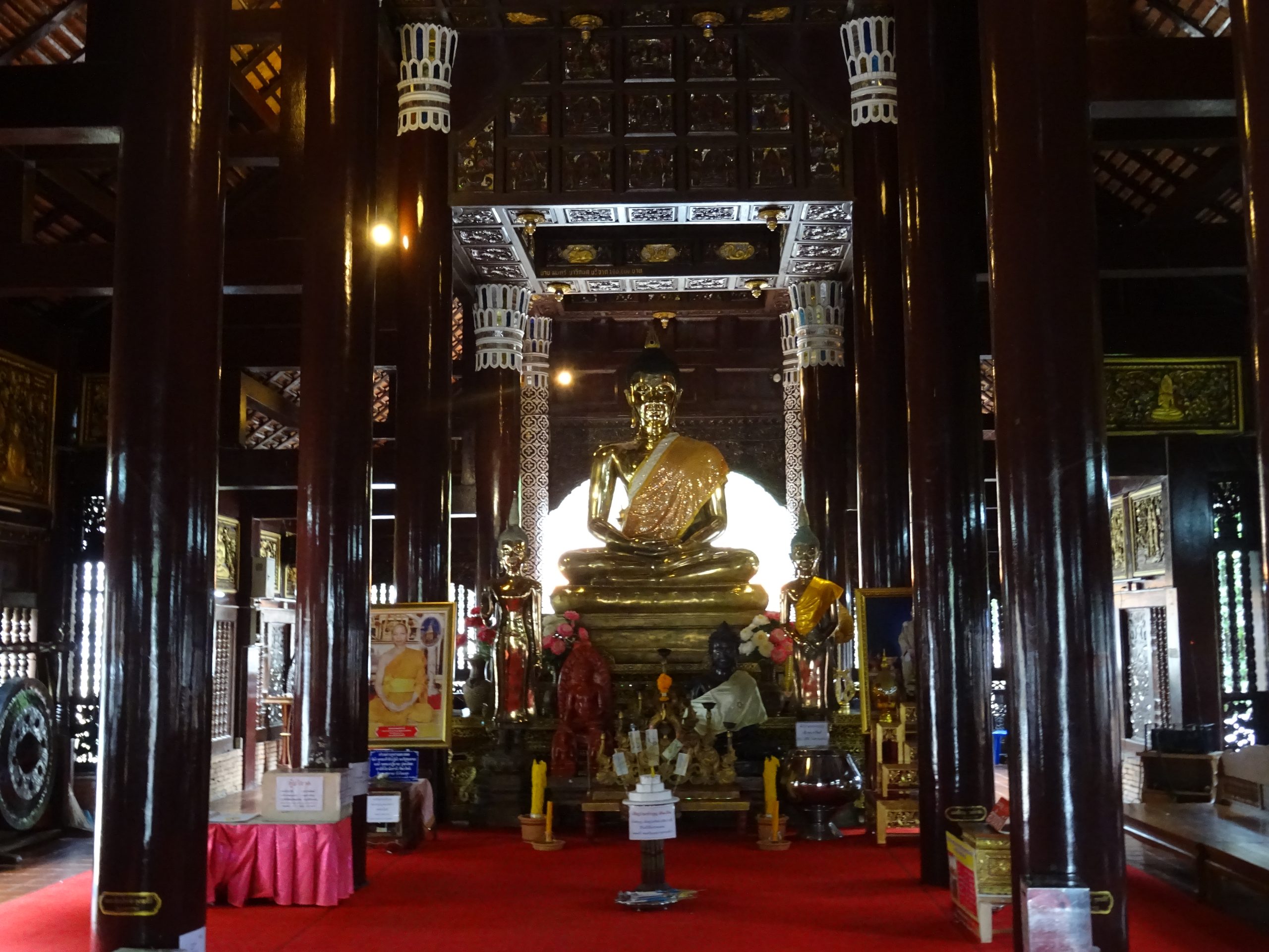 清迈 Wat Lok Moli 礼佛殿内部，深色柱列、白色柱头纹饰、金色禅定坐佛和红色地面