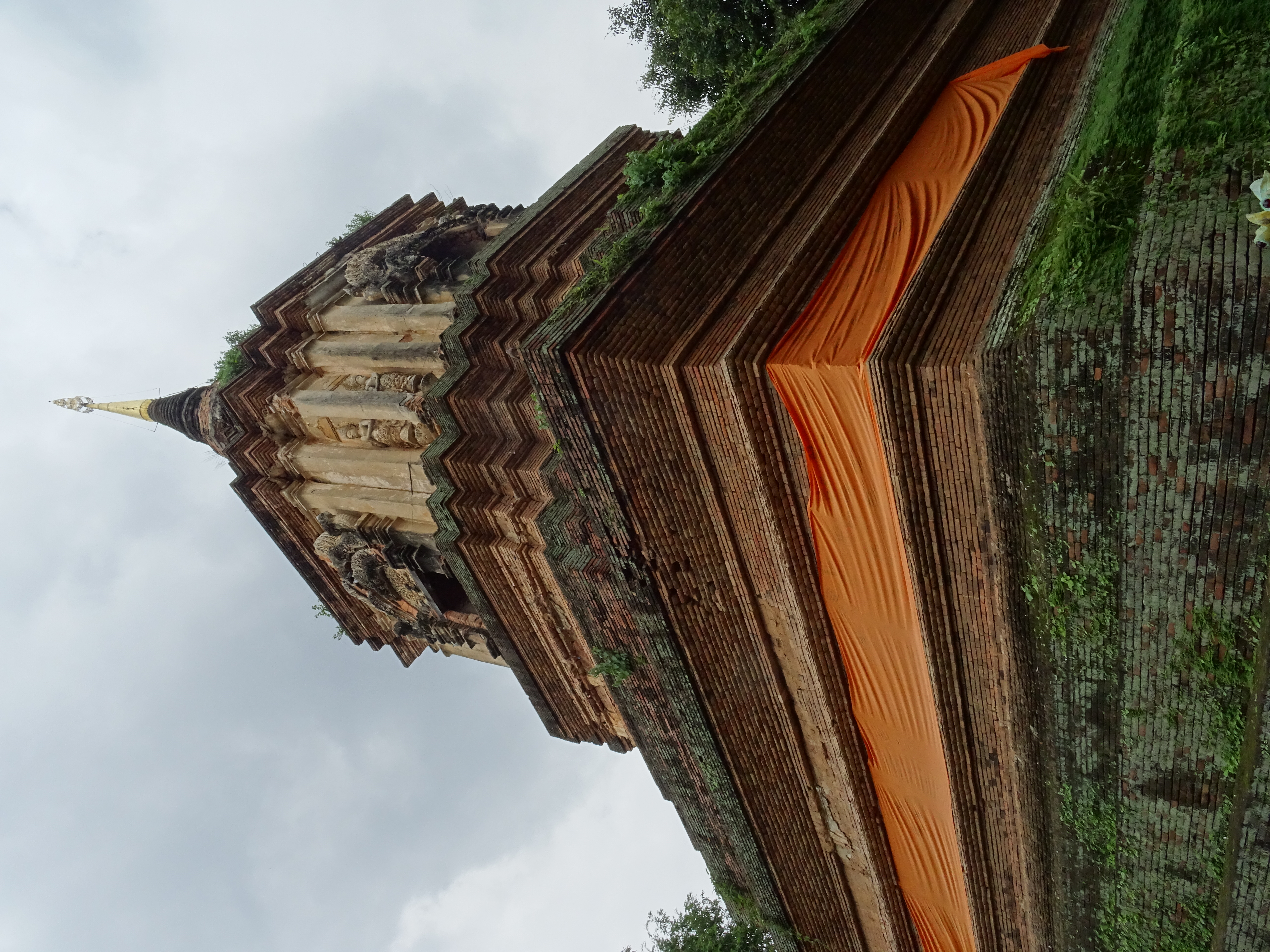 清迈 Wat Lok Moli 砖塔转角近景，橙色围布、横向砖层、浅色佛龛、转角灰塑人物与尖顶