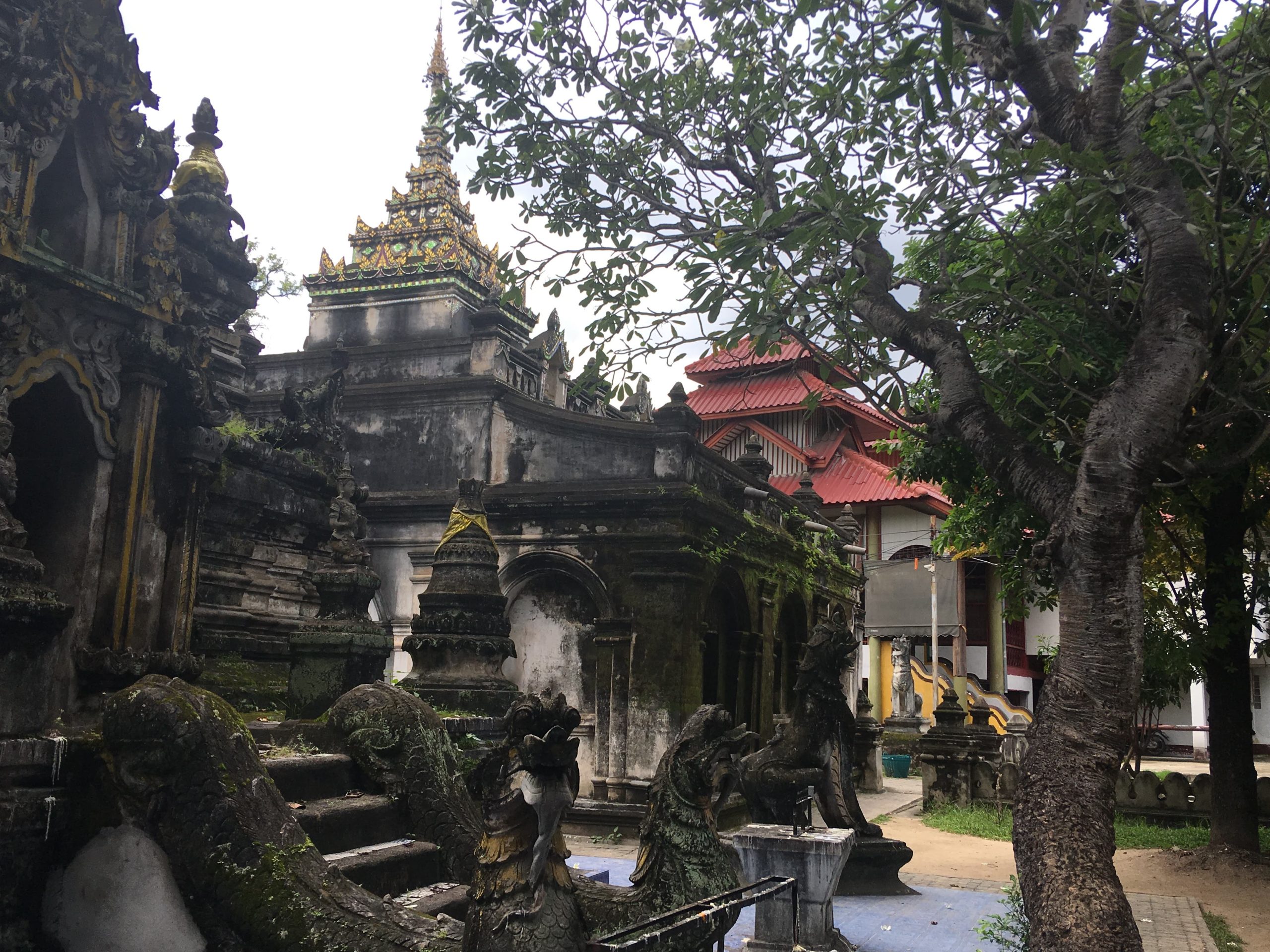 清迈 Wat Pa Pao 院内建筑,树下高台层叠尖顶、前景阶梯雕塑和后方红顶殿堂