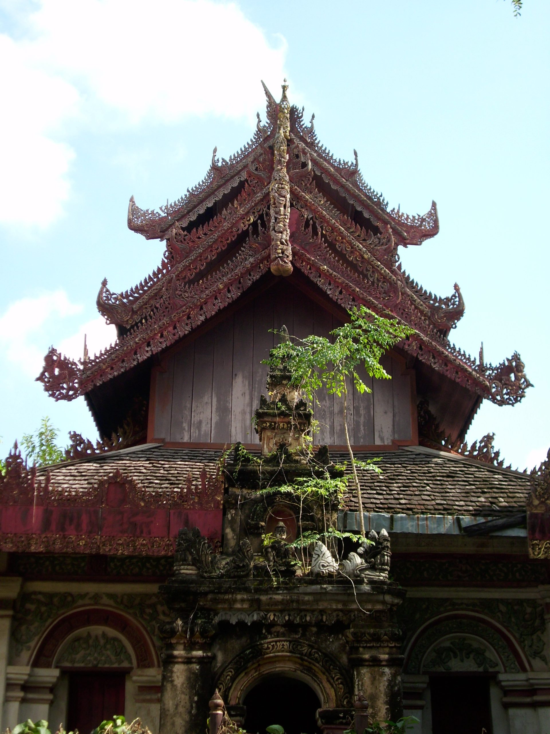 清迈 Wat Pa Pao 殿堂正面,层叠的深色木山墙、金色构件、橙红屋面及前景黄红拱形构筑物