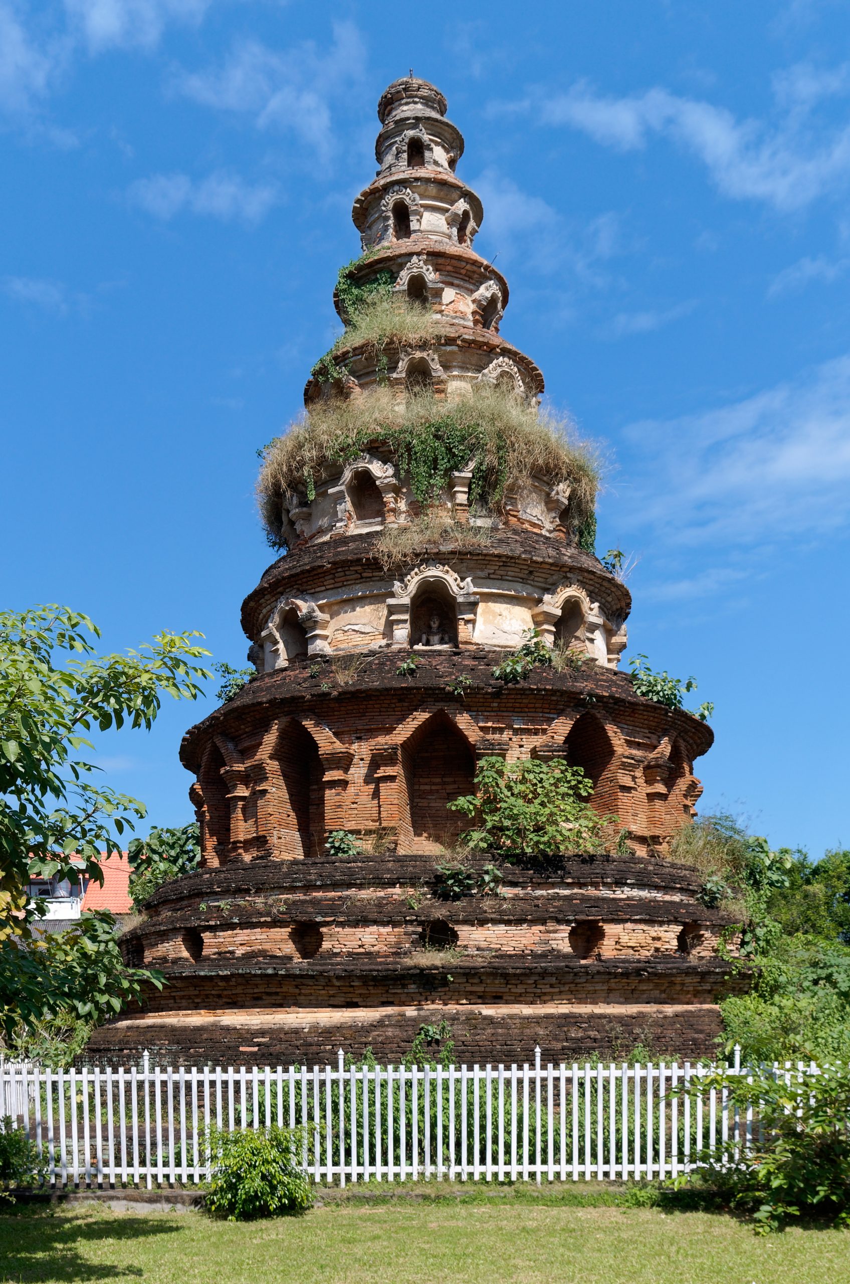 清迈 Wat Phuak Hong 圆形七层砖塔全景,层间佛龛、残存白色灰泥、塔脚围栏及草地