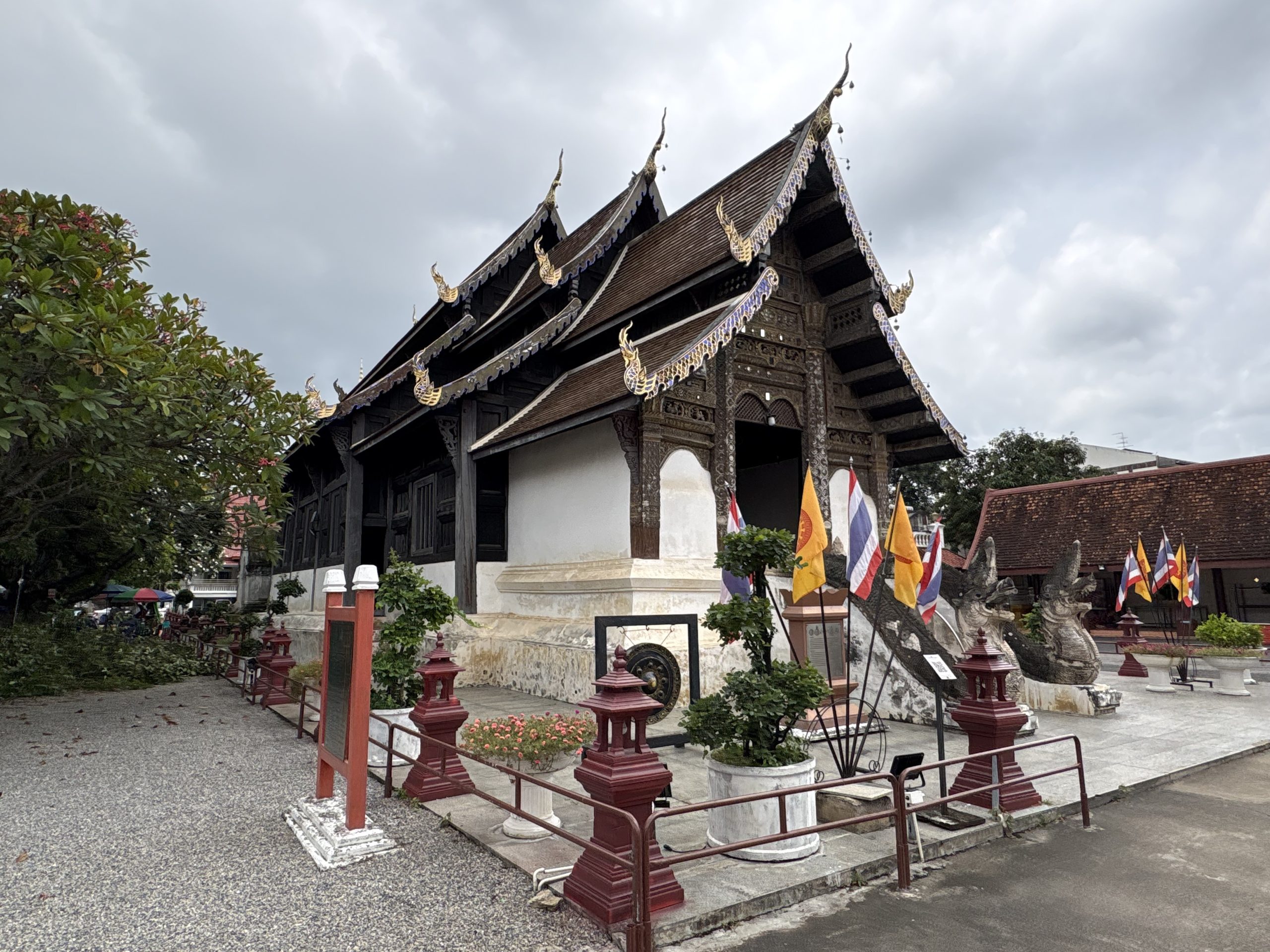 清迈 Wat Prasat 礼佛殿侧前方，分段瓦顶、深色木墙窗、白墙基与兽形台阶栏