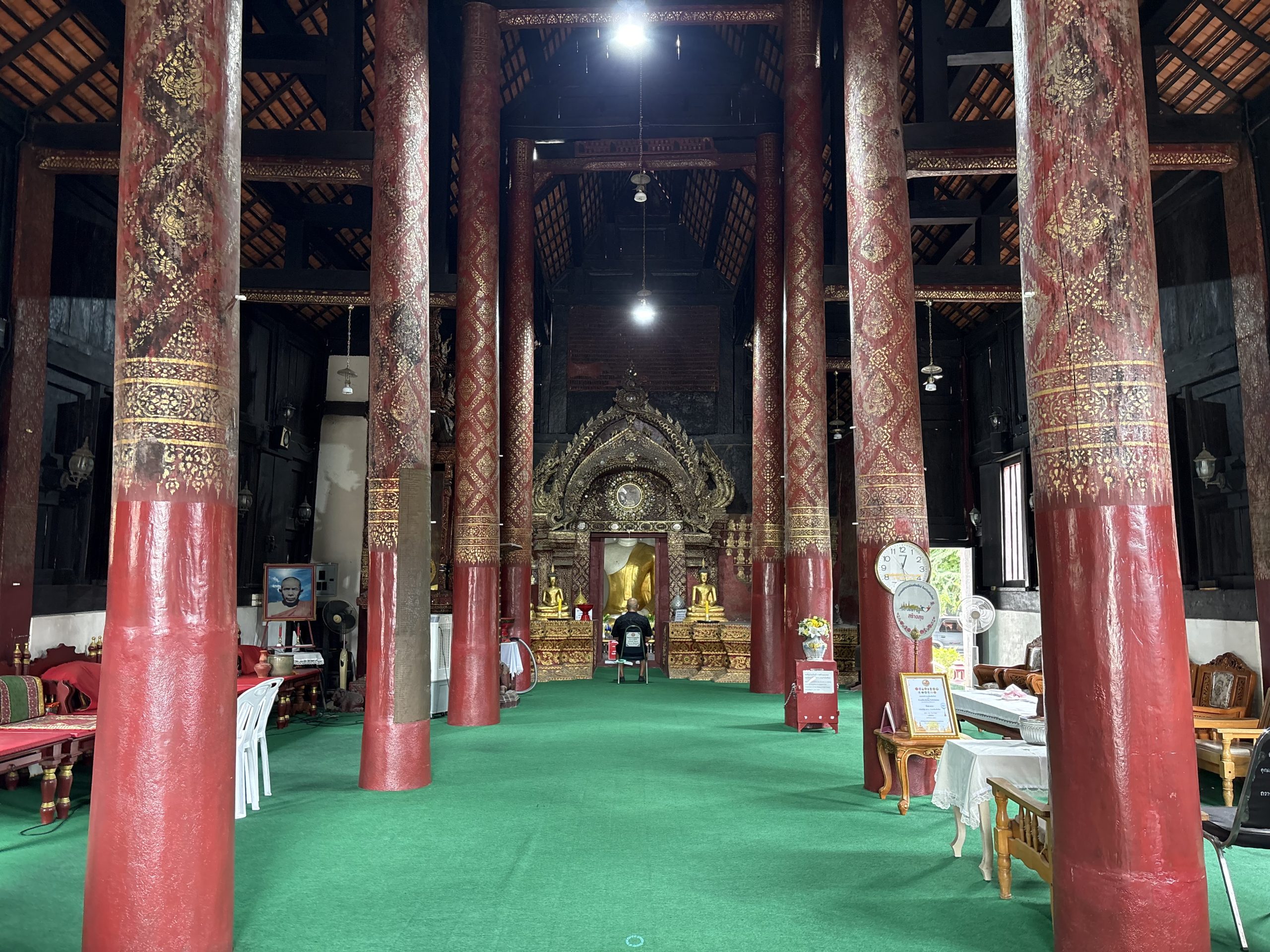 清迈 Wat Prasat 殿内红柱和金色纹样，绿色地面通向金饰拱框及开口后佛像