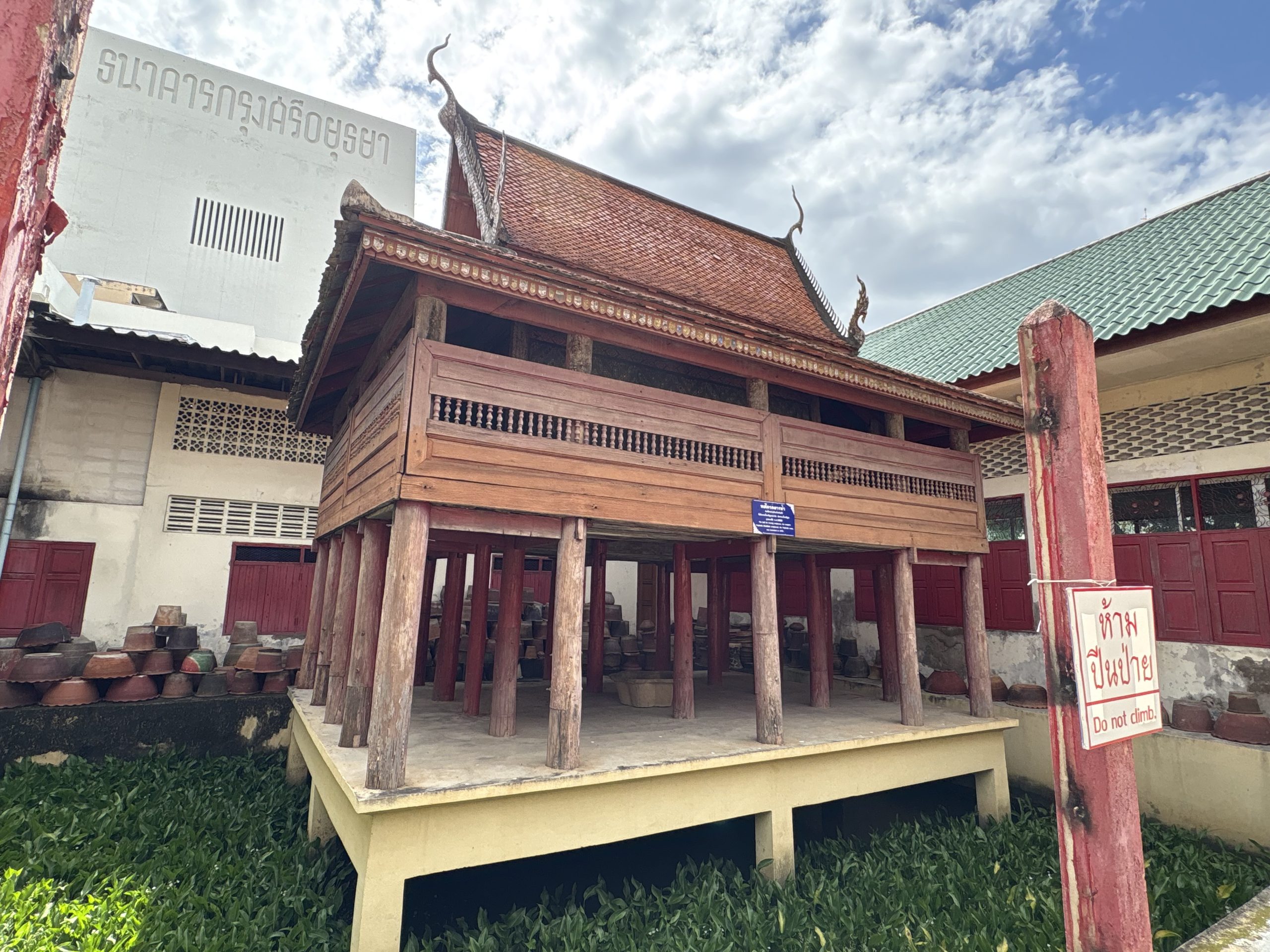 清迈 Wat Saen Fang 的架高木经楼,周围池面长满绿叶,旁边立着禁止攀爬标牌