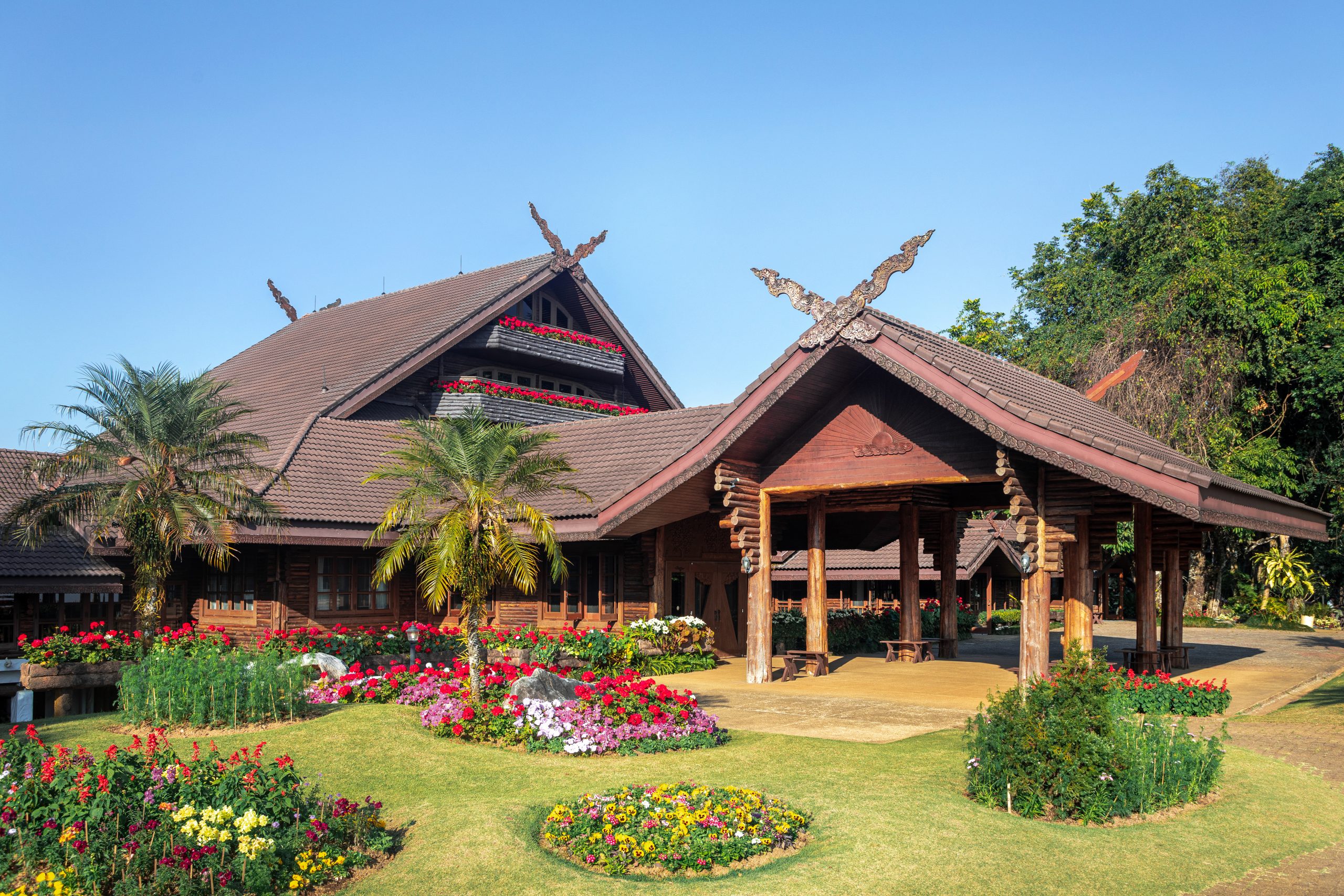 Doi Tung Royal Villa 的木构建筑、屋顶、花园和周边树木。
