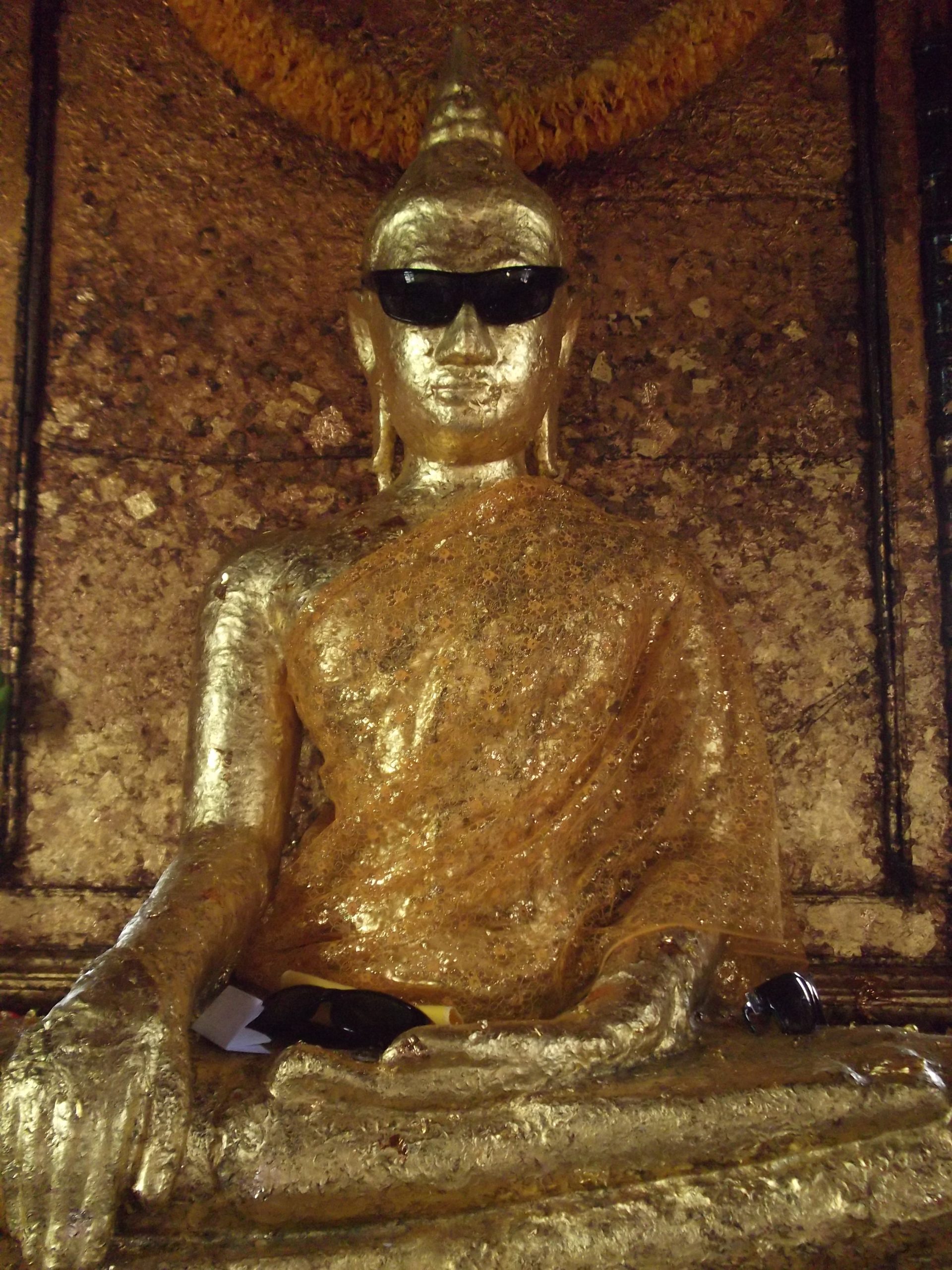 Luang Pho Pu戴着黑色墨镜，腿前也放着眼镜。