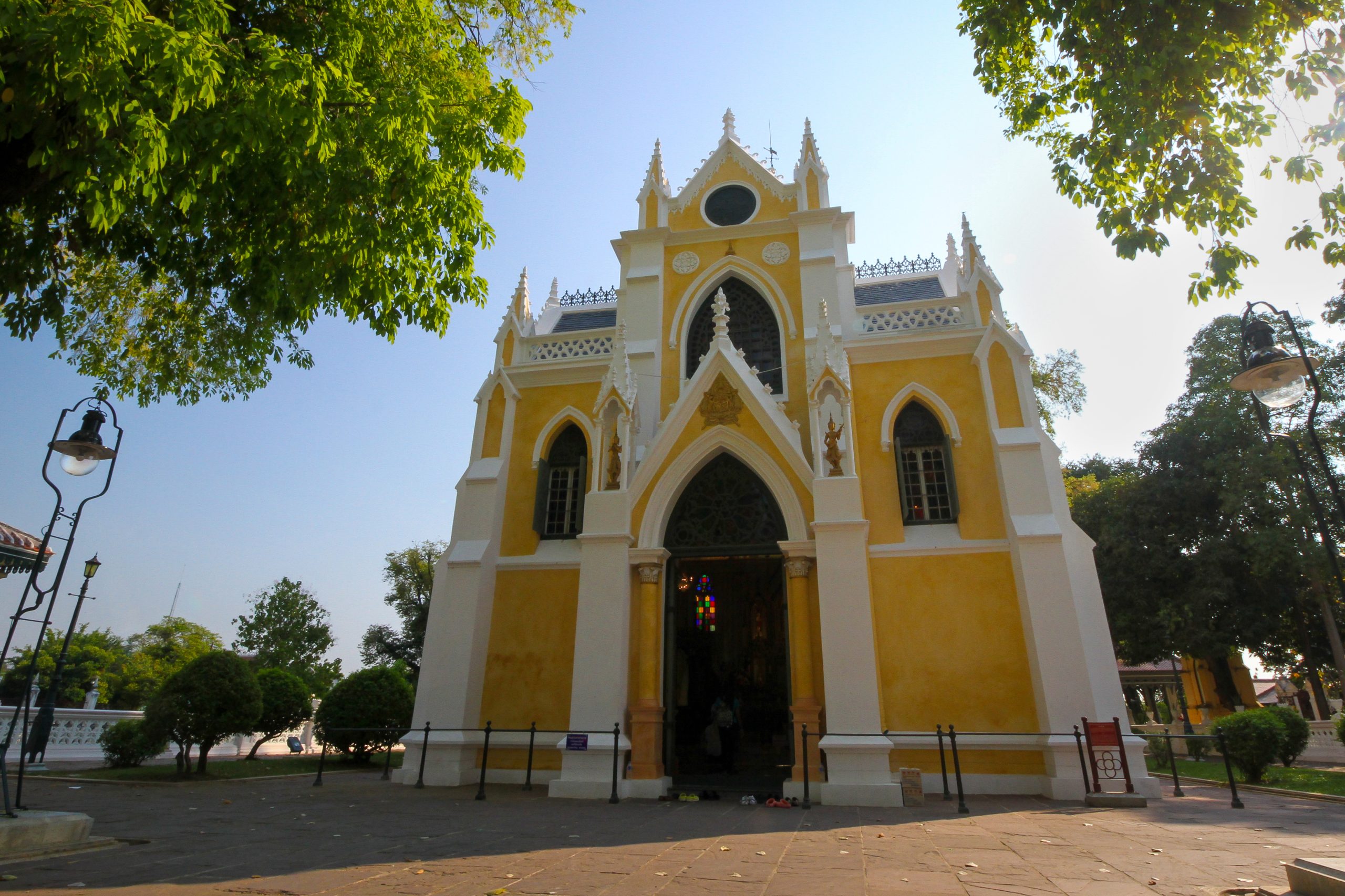 Wat Niwet Thammaprawat黄色白边戒堂正面,尖拱入口与两侧壁龛,树荫下的完整立面