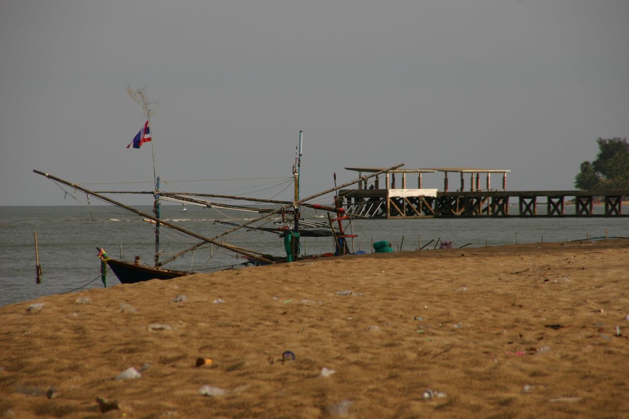 2008年Pak Nam Pran Fishing Pier附近沙地、半遮船身和船杆、小旗、水面及远处顶棚码头