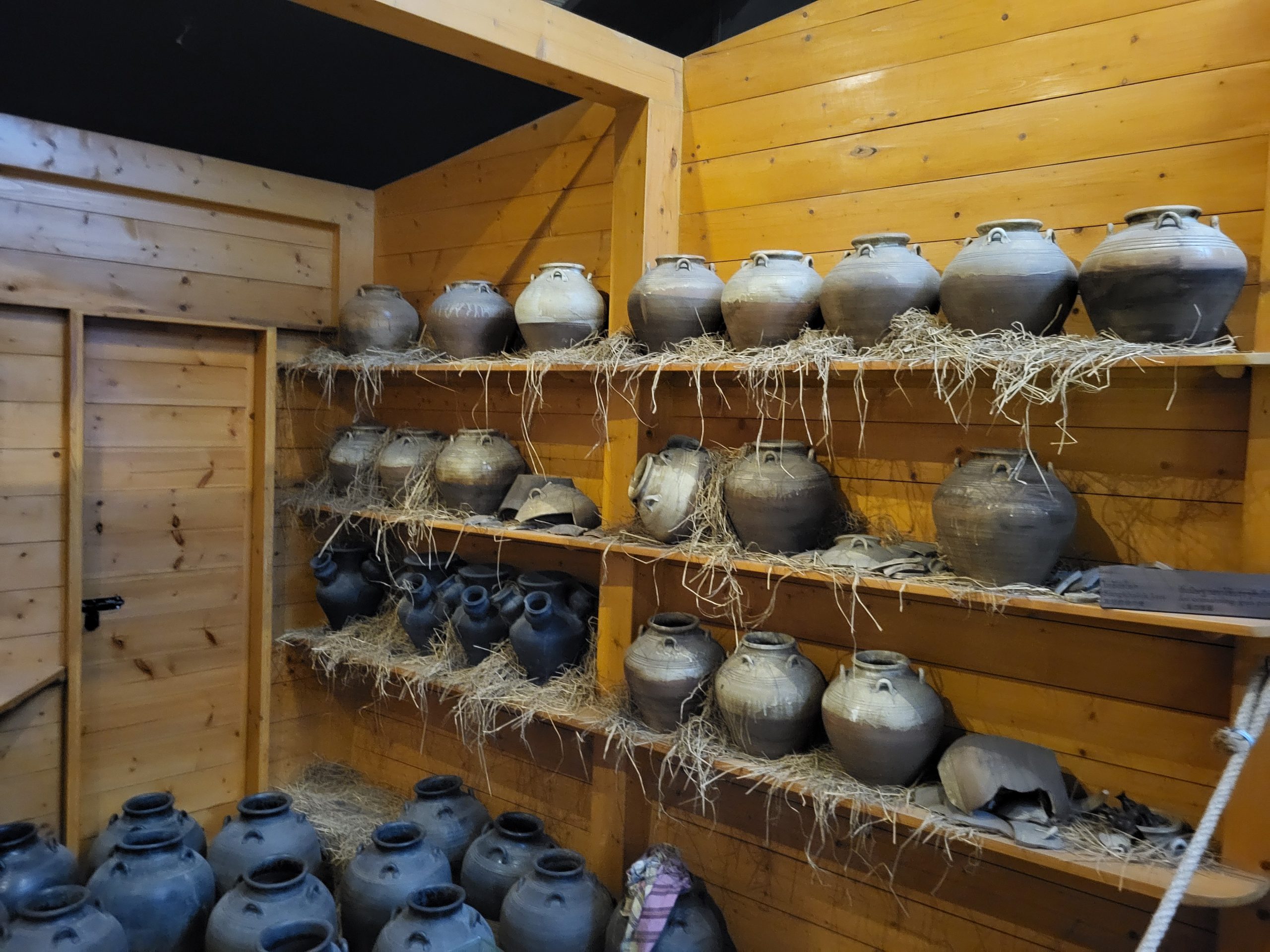 日本村馆内木板展陈空间，架子和地面摆放陶罐与碎陶片