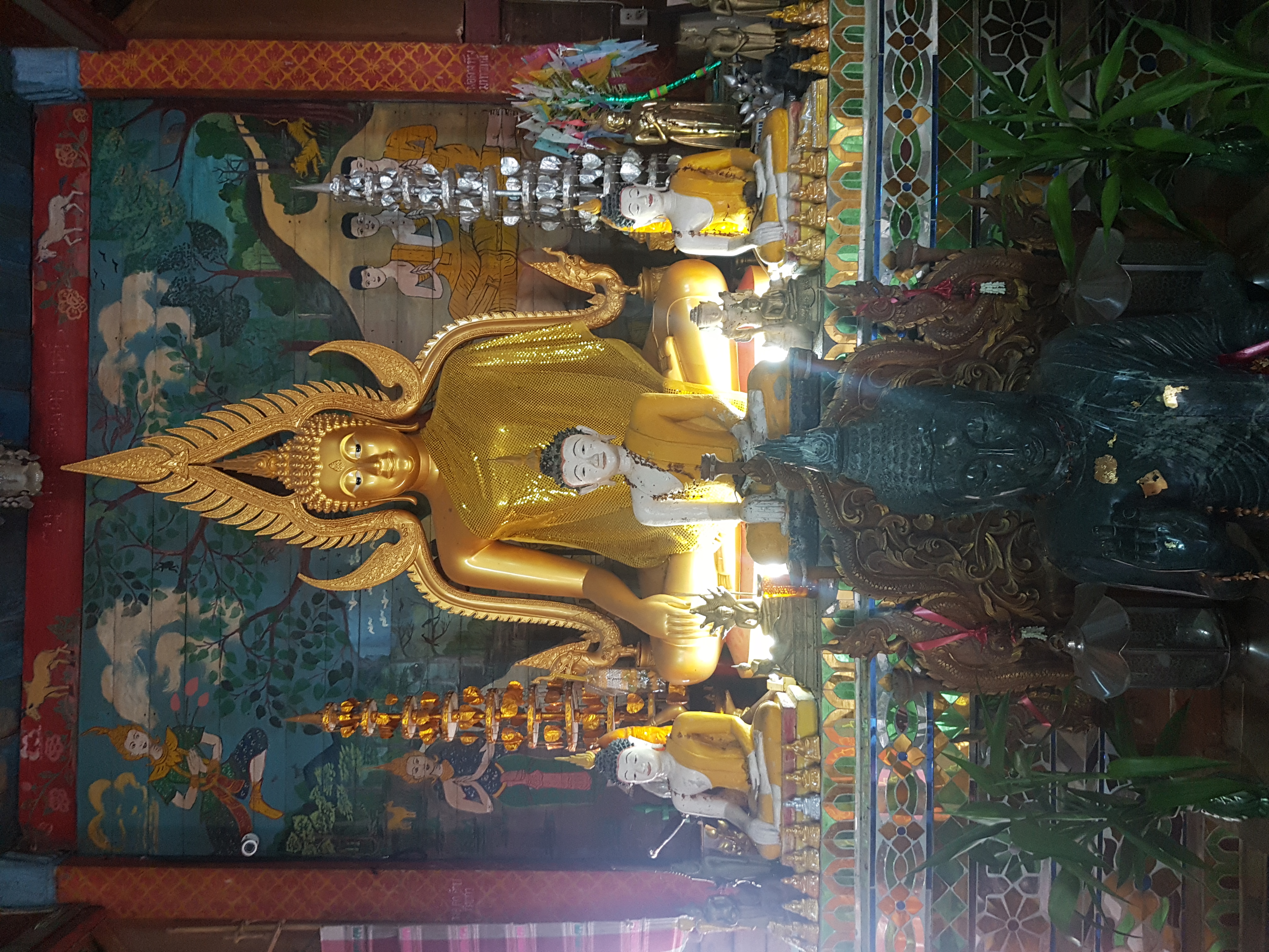 Wat Khantha Phrueksa寺院内部，金色坐佛、较小佛像和供桌后有壁画