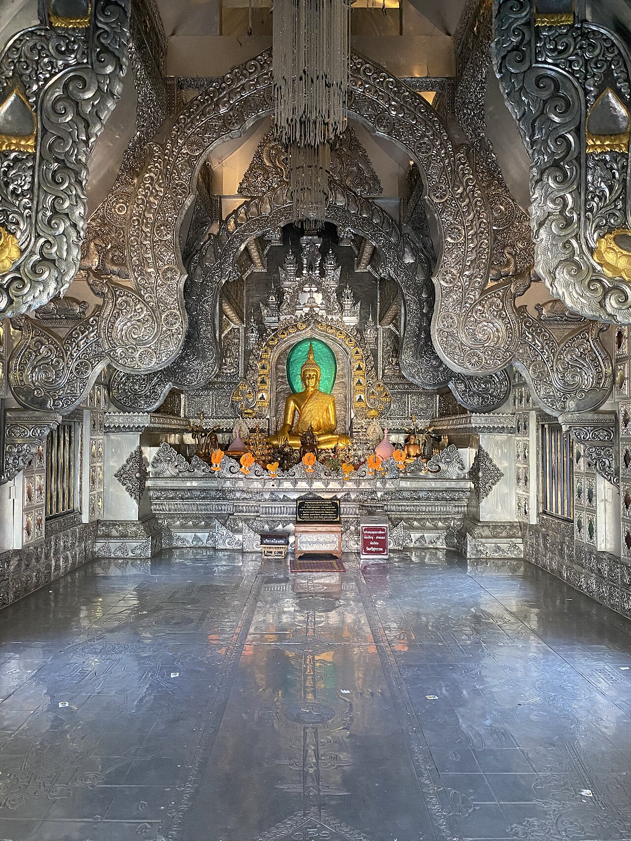 Wat Sri Suphan室内中央的金色坐佛、绿色背景、银色层叠拱饰与供桌。